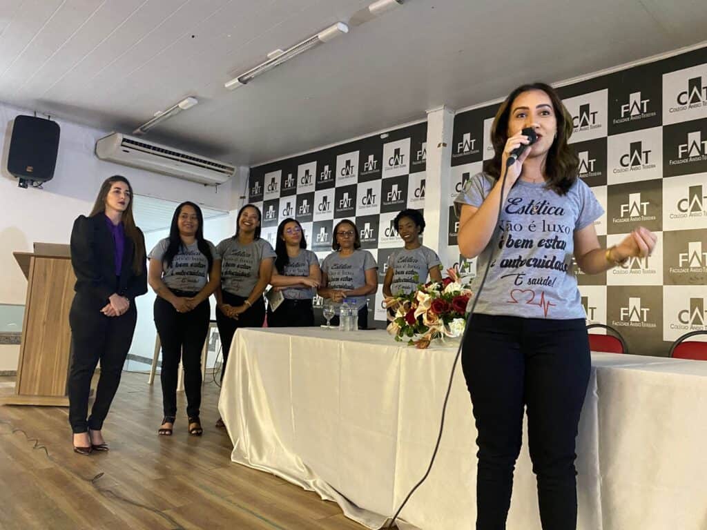 Estudante falando em evento na UNIFAT com colegas ao fundo, em ambiente acadêmico.
